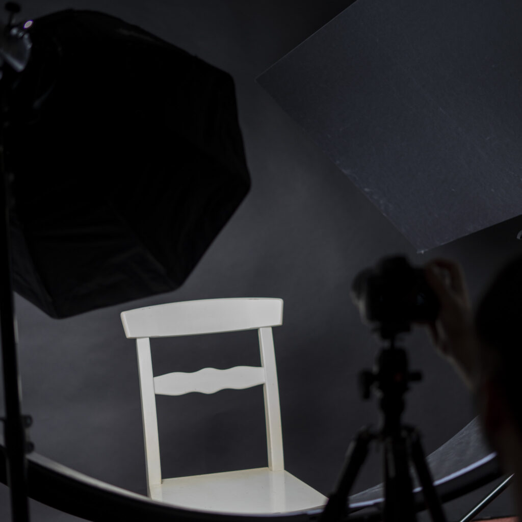 Bild einer Studioeinrichtung mit weißem Stuhl, schwarzem Hintergrund, Halfpipe-Reflektor und Blitzlicht mit Softbox.