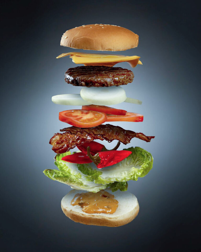 Bild eines dekonstruierten Hamburgers, bei dem alle Schichten sauber voneinander getrennt vor einem Hintergrund mit Farbverlauf und Spotlight schweben.